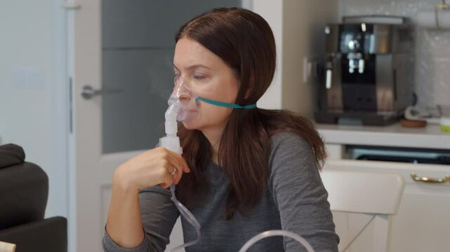 Face of adult woman during inhalation with nebulizer at home. Woman holding breathing inhaler for home procedure. Woman inhaling through inhaler mask.