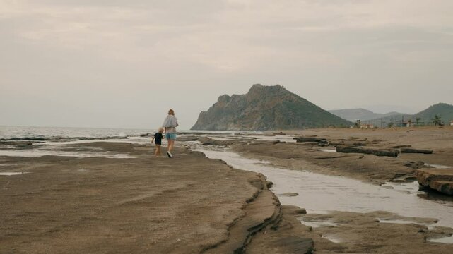 Tourist woman and baby boy walking sea beach sand stone mountain tropical landscape slow motion