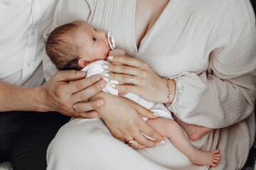 A woman is holding a baby in her arms. The baby is wearing a pacifier. The woman is wearing a white...
