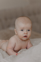 A baby is laying on a bed with a blanket. The baby is looking at the camera with a surprised expression