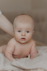 A baby is laying on a blanket with its head turned to the side. The baby's face is looking up at the camera, and its eyes are wide open. The baby's head is bare, and its body is covered in a blanket
