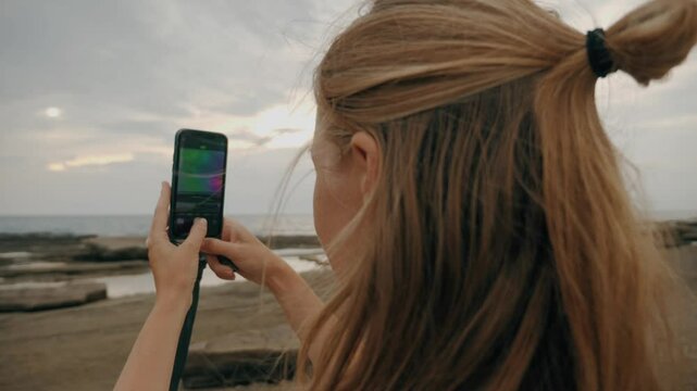 Redhead travel woman making photo dramatic sky sea beach seaside landscape on smartphone camera