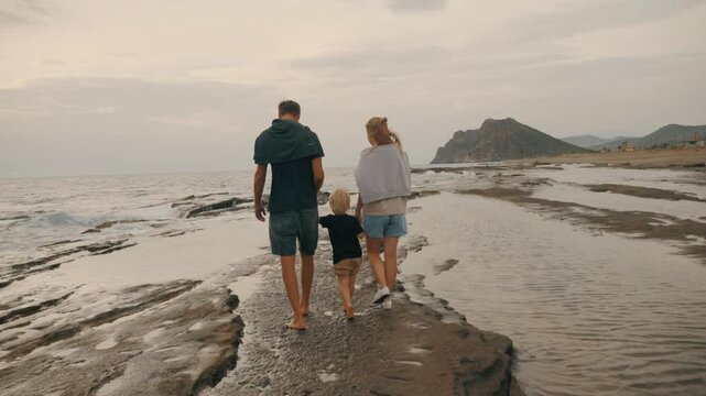 Man woman and child walking seaside tropical resort sea foamy wave holding hands back view slowmo