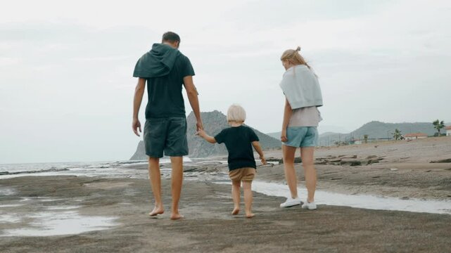 Travel mother father and boy son walking together on sea beach holding hands slow motion