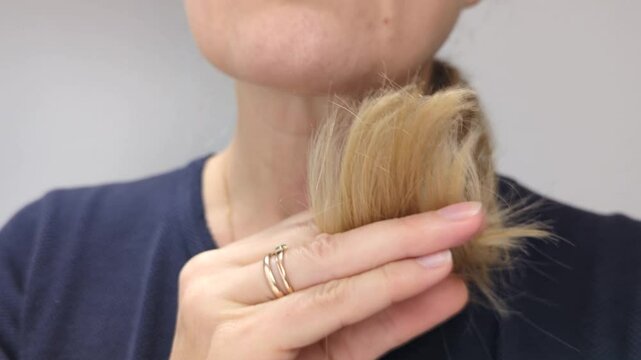 Middle-aged blonde European woman carefully examines the condition of her hair. She is concerned about the dullness of her hair, the loss of volume and split ends.
