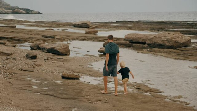 Father and son holding hands walking sea sand pebble cliff beach wave coastline scenery slow motion