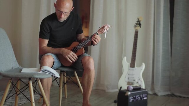Ukulele string instrument video popular on Hawaii islands. Man playing nylon strings during music self-teaching lessons in living room electric guitar backdrop Musical education and art people concept