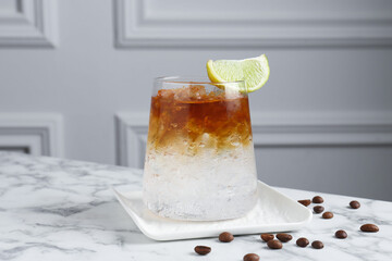 Refreshing espresso tonic drink with slice of lime and coffee beans on white marble table
