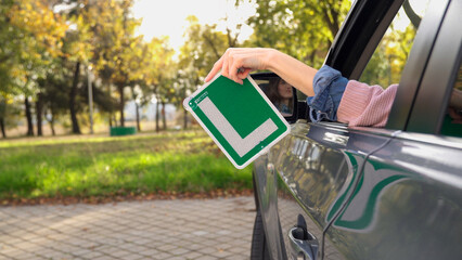 Young driver holding learner plate out of car window