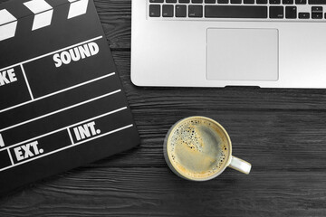 Movie clapper, laptop and cup of coffee on black wooden table, flat lay