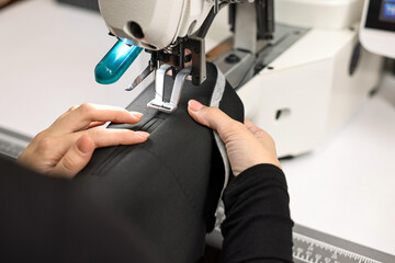 Woman working with sewing machine at white table in professional workshop, closeup