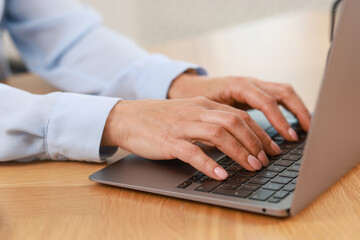 Office worker typing on laptop at wooden table, closeup