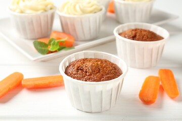 Delicious carrot muffins and fresh vegetables on white wooden table, closeup