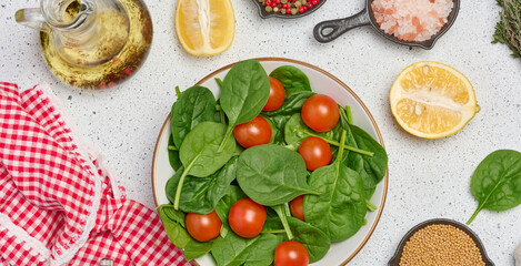 Salad of spinach leaves and cherry tomatoes in a round white plate on a white background, top view
