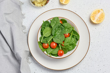 Salad of spinach leaves and red cherry tomatoes. Top view on a white table