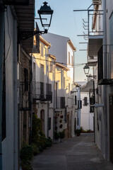 Calle estrecha y pintoresca de un pueblo español, con casas blancas y balcones de hierro forjado, iluminada por la luz del atardecer. Iznatoraf, Jaén, Andalucía, España