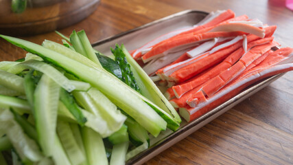 Cucumber cut into strips and crab sticks lie in a rectangular plate on a wooden table © mikus