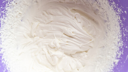 White whipped cream. Whipped cream in a purple plastic bowl