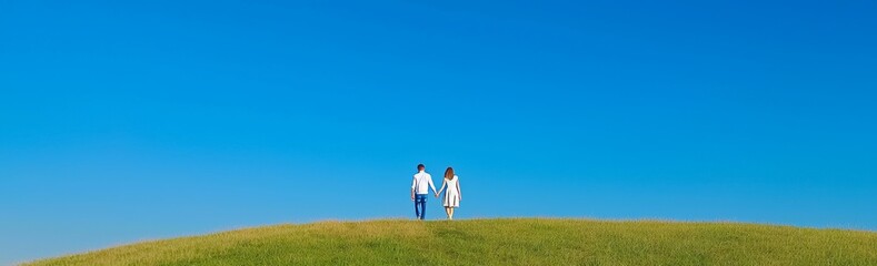 A couple in love holds hands as they walk across a grassy slope, accompanied by a banner.