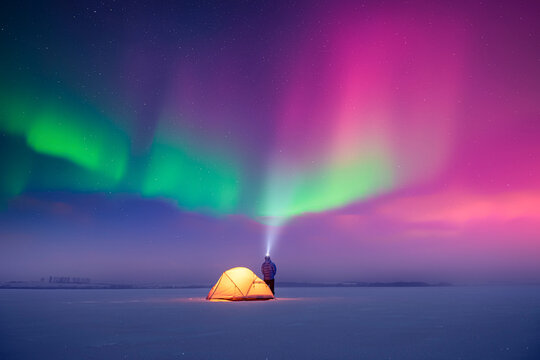 Tourist shines a flashlight in incredible starry sky with Aurora borealis. Gorgeous night landscape with polar lights and yellow tent. Northern lights in winter field - Powered by Adobe
