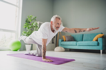 Elderly man practicing yoga in bright living room, maintaining fitness and healthy lifestyle