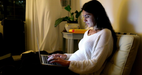 Woman working from home in front of laptop. Person typing on her computer at night