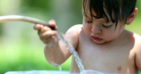 Toddler boy playing with water hose outdoors during summer day inside bucket