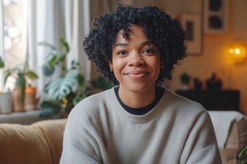Fototapeta premium Smiling woman with curly hair sits comfortably in a cozy living room with plants and warm lighting in the background