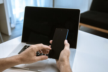 Hands using smartphone. Man working with computer laptop, black display. New technology concept
