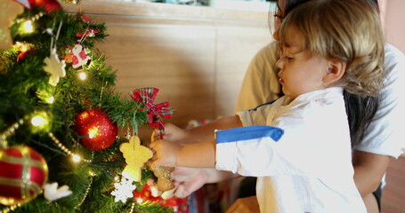 Little toddler boy decorating christmas tree with mother