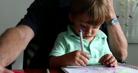 Naklejka premium Little toddler boy doodling on paper while sitting on grand-father lap