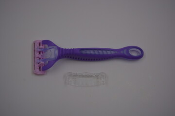Objects for female beauty, things for the omission of everyday life. A purple, sporty plastic shaving machine is located on a white plastic background.