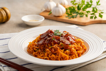 Hot and spicy Korean flavour Stir Fried instant noodle in white plate.topped with bacon and sesame seed.Asian food.