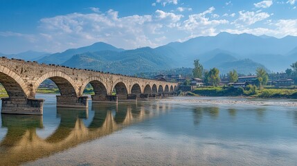 Fototapeta premium The ancient stone rice bridge stands strong over the river, its worn edges hinting at centuries of history.