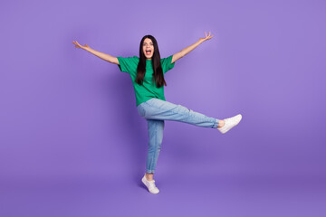 Joyful young woman in casual style posing with arms outstretched and a wide smile on a vibrant purple backdrop