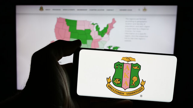 Stuttgart, Germany - 11-26-2024: Person holding mobile phone with logo of US Alpha Kappa Alpha Sorority Inc. (&Alpha;&Kappa;&Alpha;) on screen in front of web page. Focus on phone display.