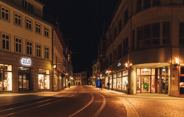 night view of quiet european street with tram tracks illuminated by warm lights and storefronts during winter. High quality photo