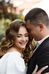 woman and man standing close to each other and smiling. A woman with long light brown hair styled in curls is wearing a white dress.