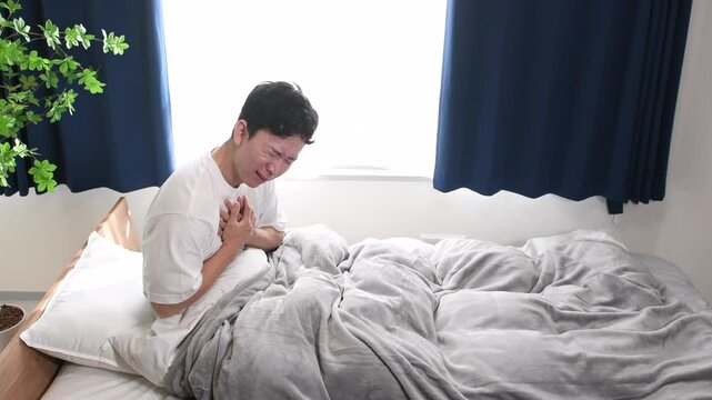 寝室で胸を抑えて苦しむ若いアジア人男性