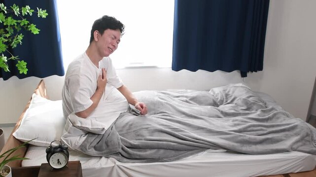 寝室で胸を抑えて苦しむ若いアジア人男性