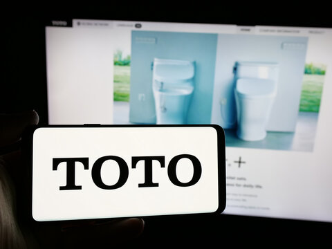Stuttgart, Germany - 11-28-2024: Person holding smartphone with logo of Japanese toilet manufacturing company Toto Ltd. on screen in front of website. Focus on phone display.