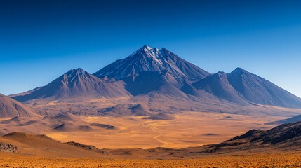 Majestic snow-capped volcano dominates arid, expansive desert landscape under a vibrant blue sky.