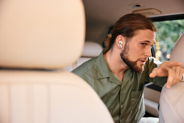 A man with earbuds sitting in a car and gesturing while speaking