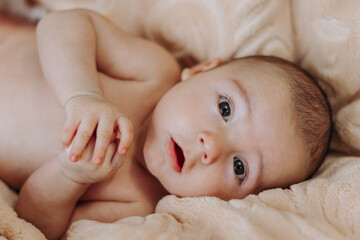 A baby is laying on a blanket with its eyes open and looking at the camera. The baby's face is full of innocence and curiosity, and the scene conveys a sense of warmth and tenderness