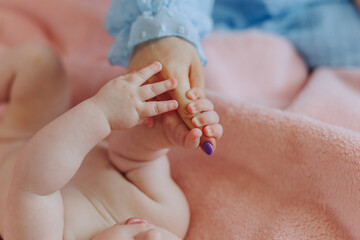 A baby is being held by a woman's hand. The baby is laying on a pink blanket