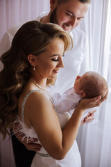 A woman is holding a baby in her arms while a man looks on. The scene is likely a family portrait or a special moment between the couple and their child. Scene is warm and loving