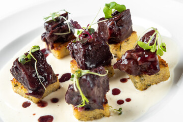 A gourmet dish featuring tender meat pieces on a bed of crispy polenta squares, drizzled with rich sauce and garnished with fresh microgreens. Perfect for food photography and culinary uses.