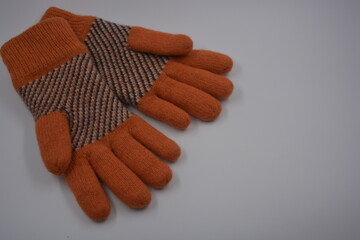 Warm, soft, winter items and household items. Beautiful orange, gray, insulated, knitted gloves are located on a white plastic background.