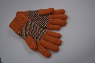 Warm, soft, winter items and household items. Beautiful orange, gray, insulated, knitted gloves are located on a white plastic background.