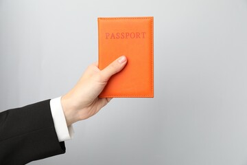 Woman holding passport in bright cover on grey background, closeup. Space for text